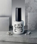 White bottle labeled 'Top Beton No Wipe' with a tall black cap sits on a gray stone surface, surrounded by small rocks.